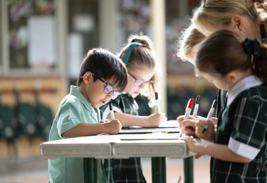 Preparatory students learning outdoors, drawing on paper spread across an outdoor table.