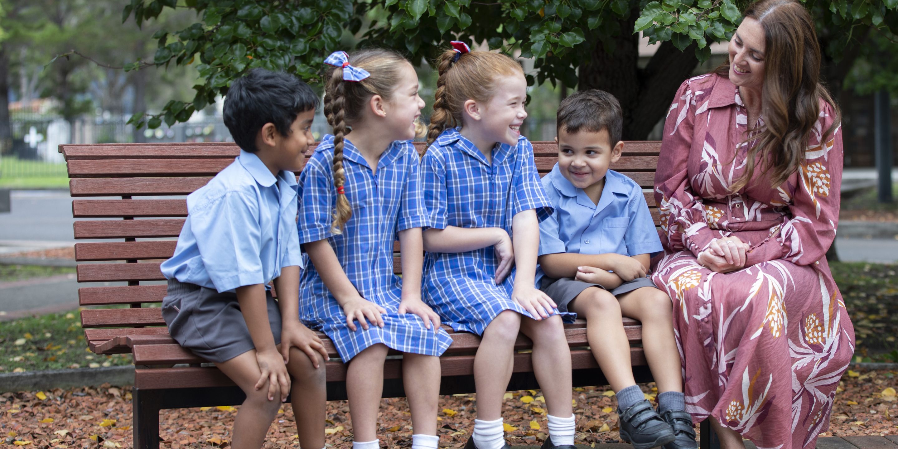 Primary school students sitting on bench with teacher.