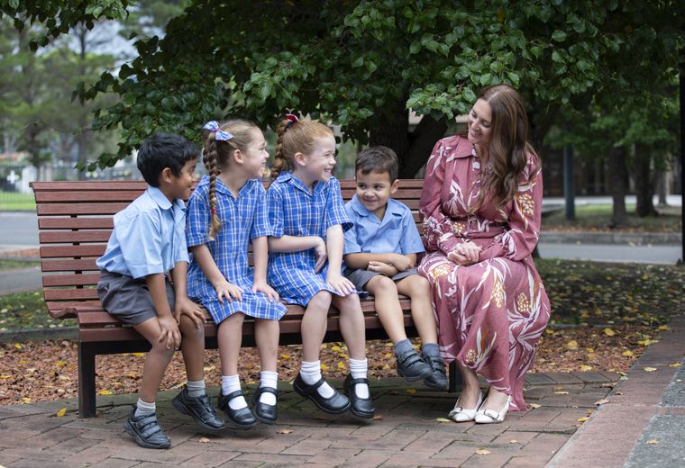 Primary school students sitting on bench with teacher.