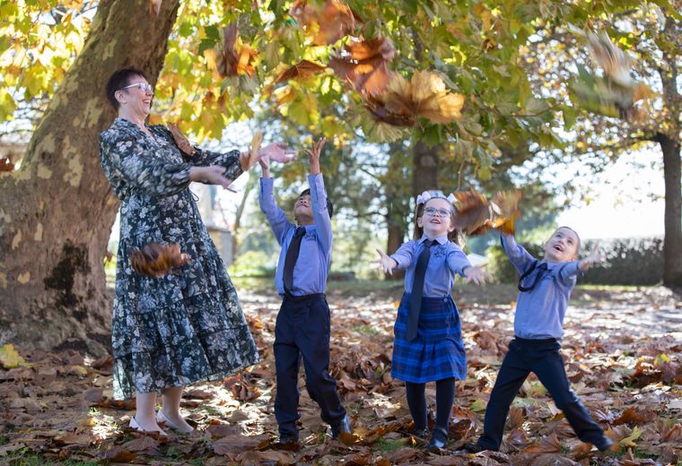 Primary school students throwing autumn leaves in air with principal.