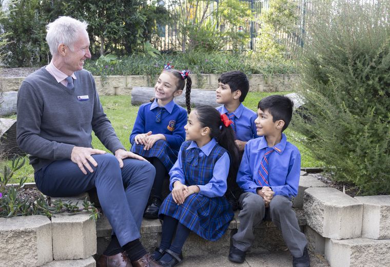 Primary school students sitting outdoors with teacher.