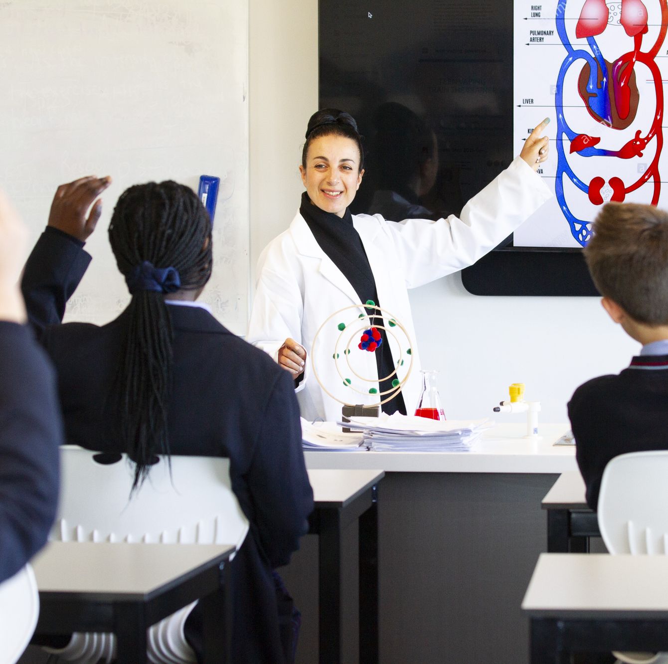 Students sitting at desk with hands raised.