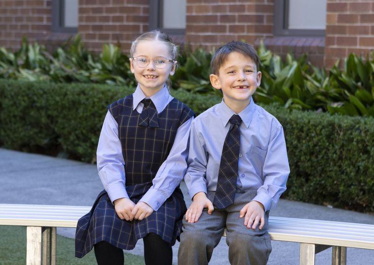 Primary school students sitting on bench outdoors.