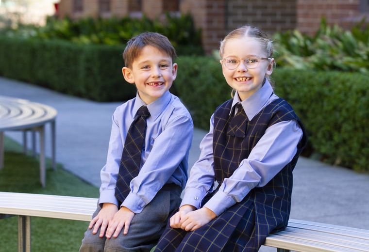 Primary school students sitting on bench outdoors.