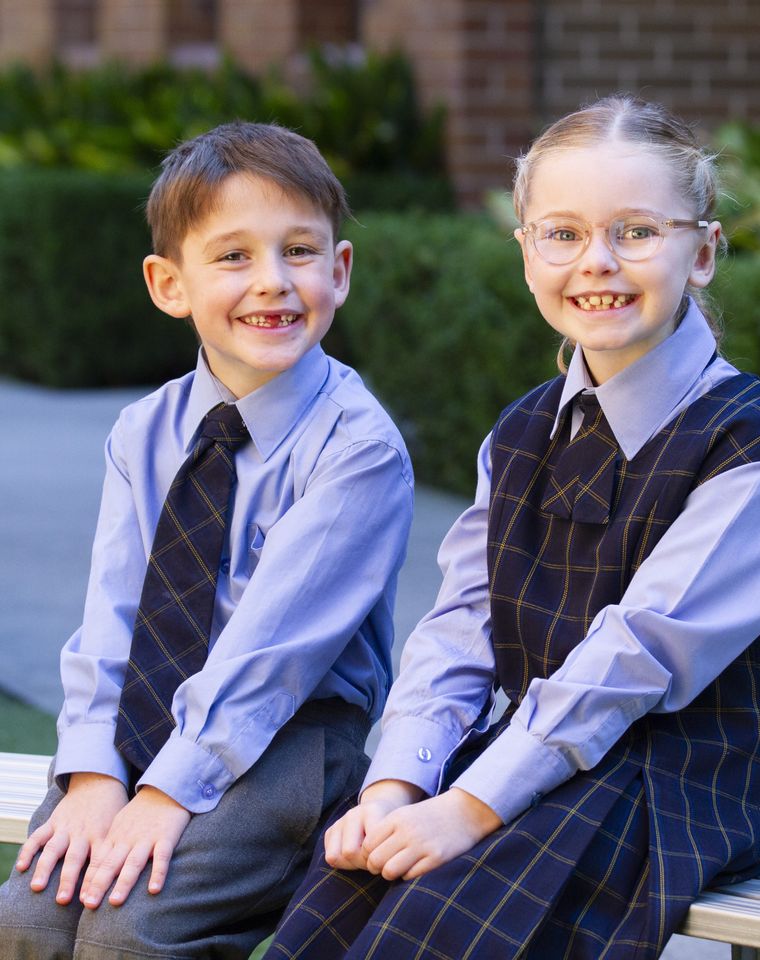 Primary school students sitting on bench outdoors.