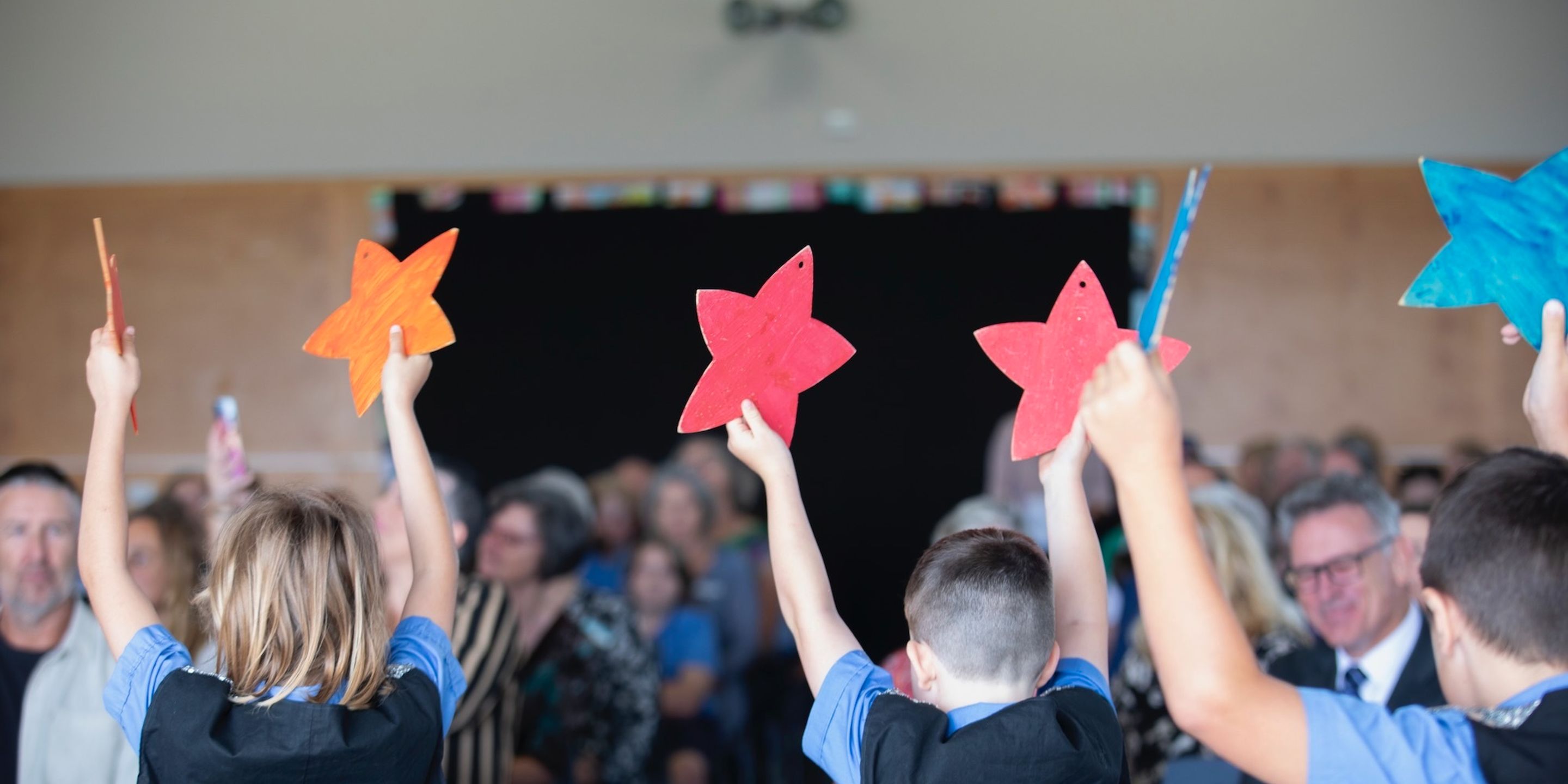 Primary school students holding up colourful paper stars.