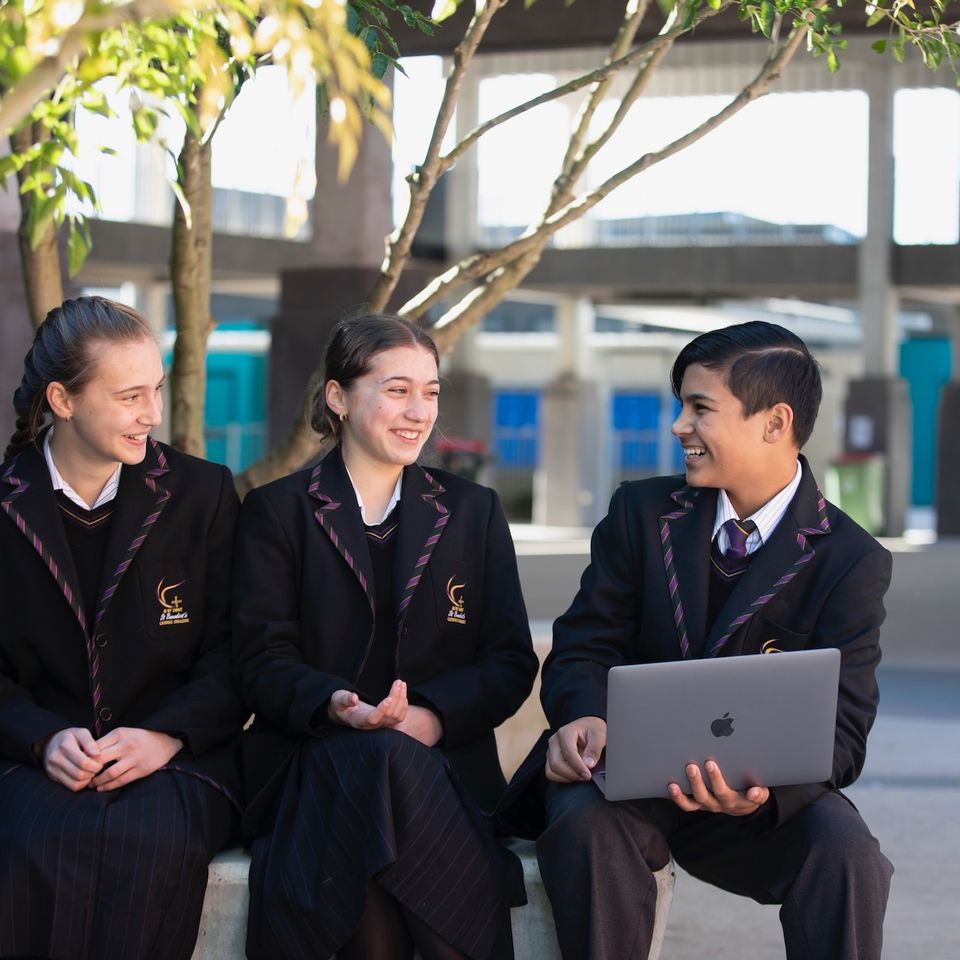 High school students sitting outdoors with laptop.