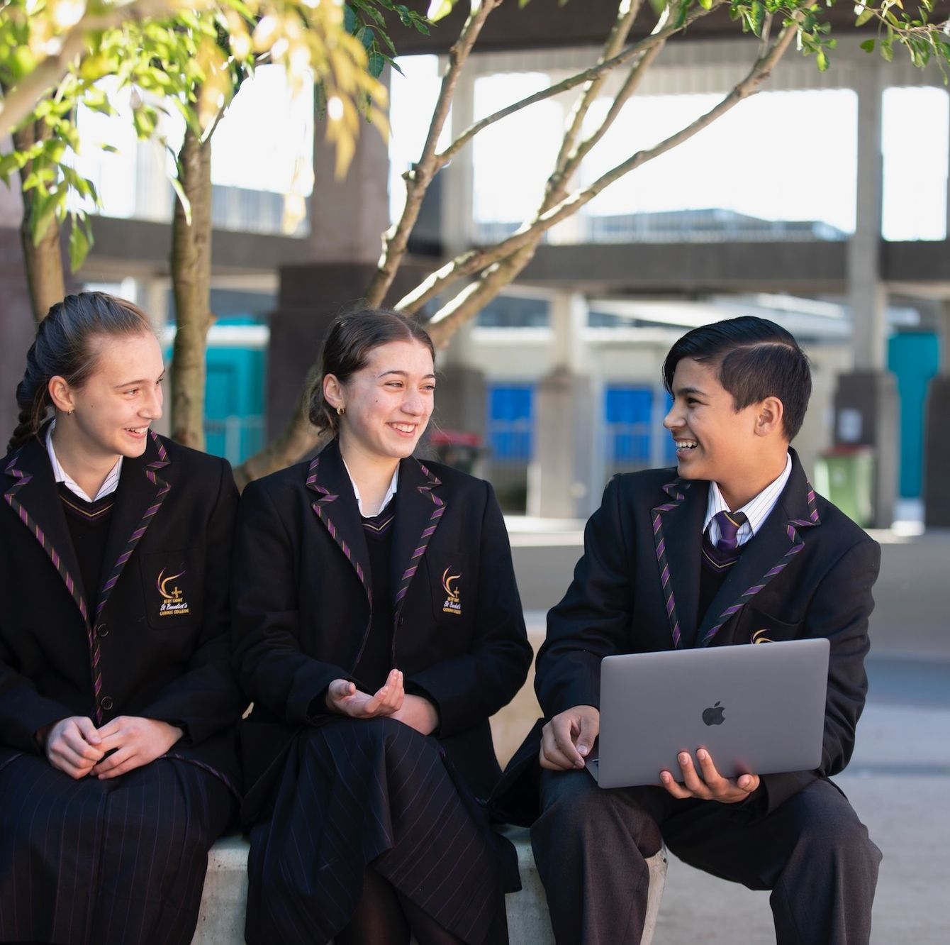 High school students sitting outdoors with laptop.