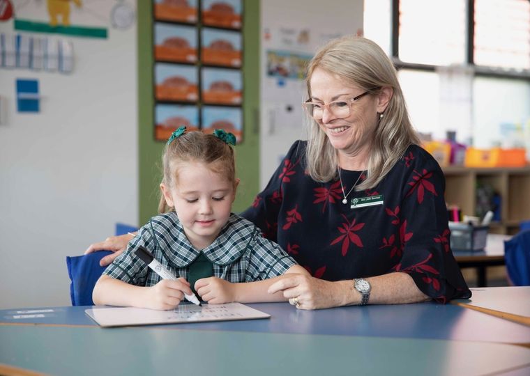 Primary school student doing schoolwork at desk with teacher.