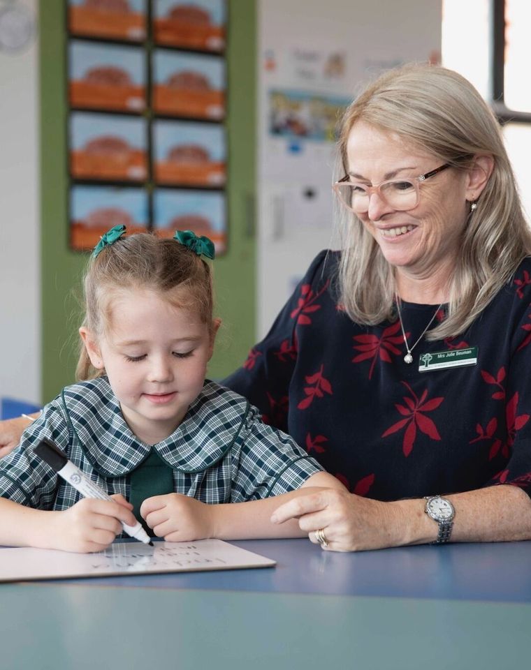 Primary school student doing schoolwork at desk with teacher.