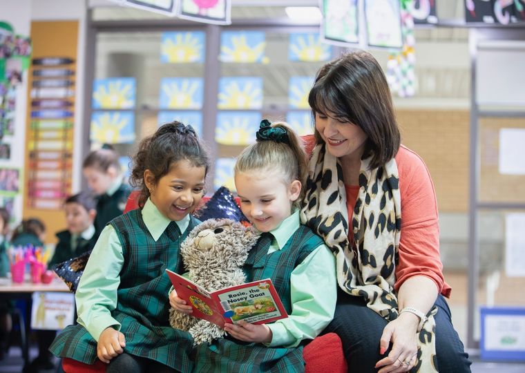 Primary school students reading a book with teacher.