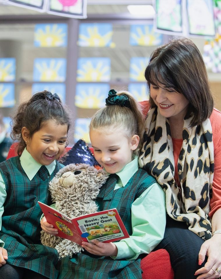 Primary school students reading a book with teacher.