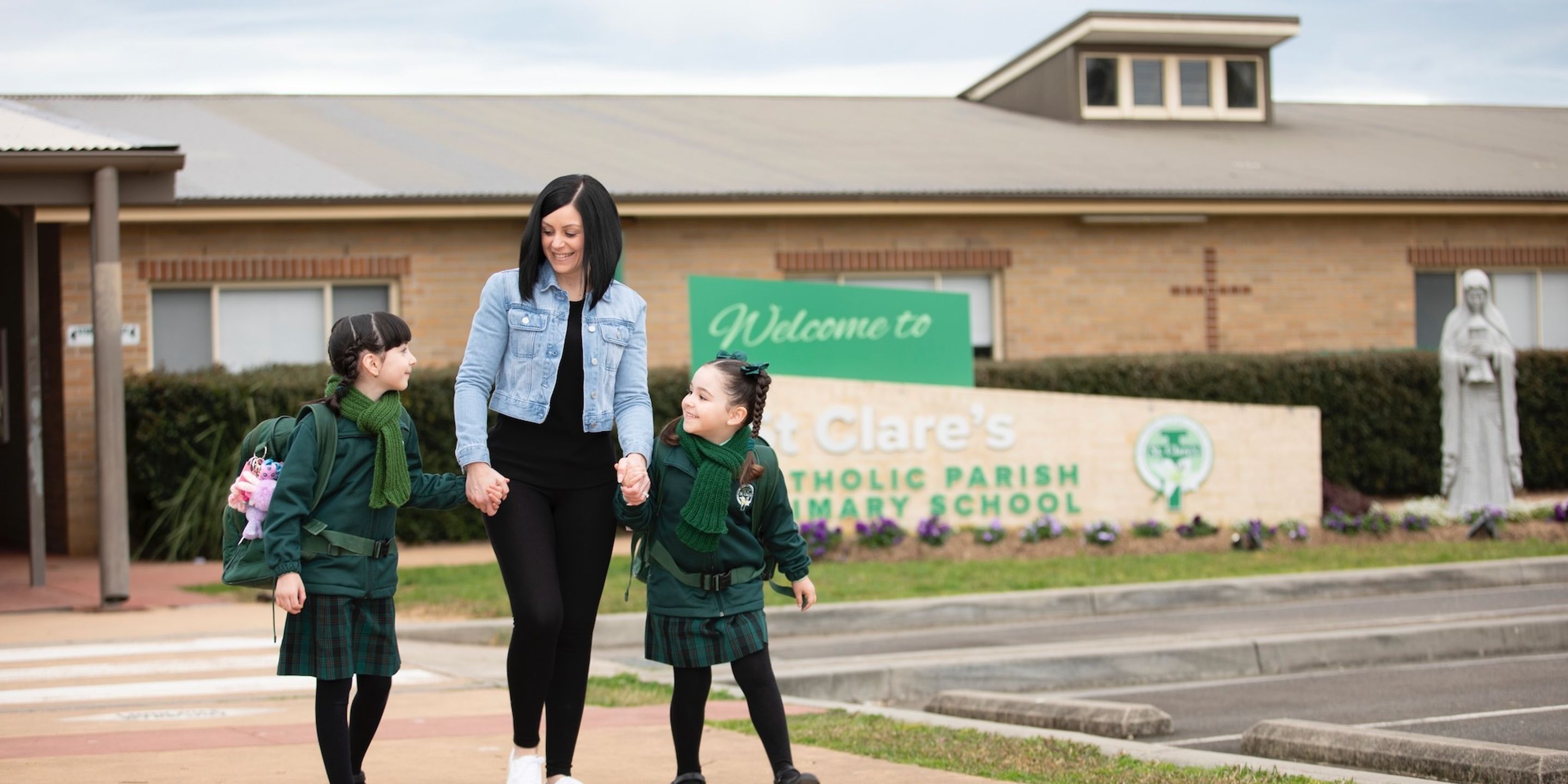 Primary school students walking outside school with parent.