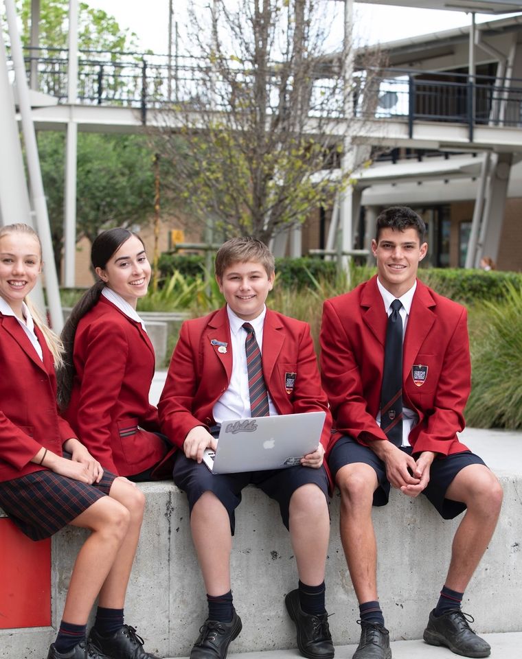 High school students sitting on bench outdoors with laptop.