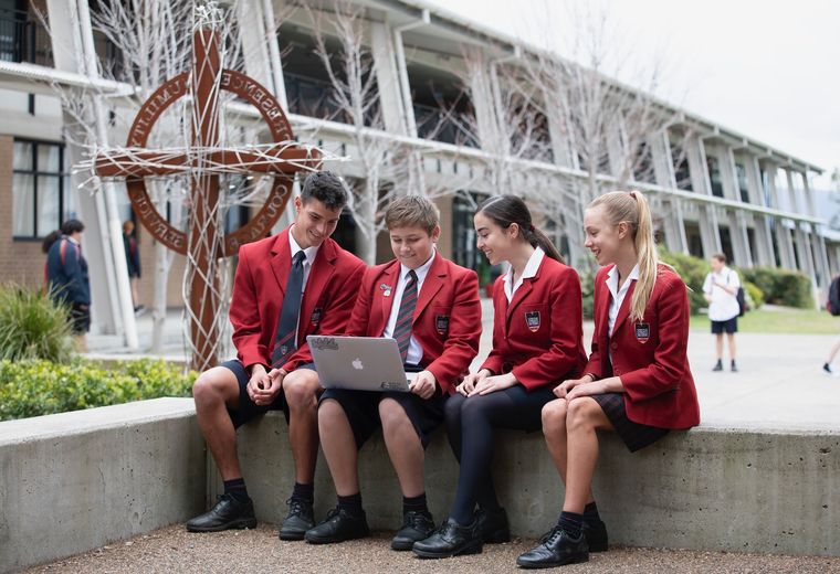 High school students sitting on bench outdoors with laptop.