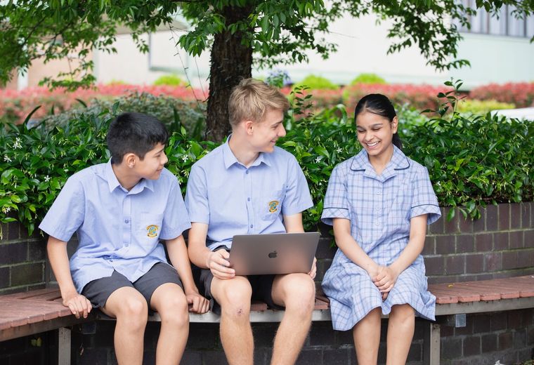 High school students sitting on bench outdoors with laptop.