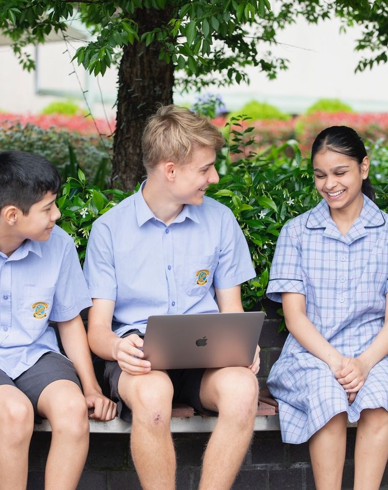 High school students sitting on bench outdoors with laptop.