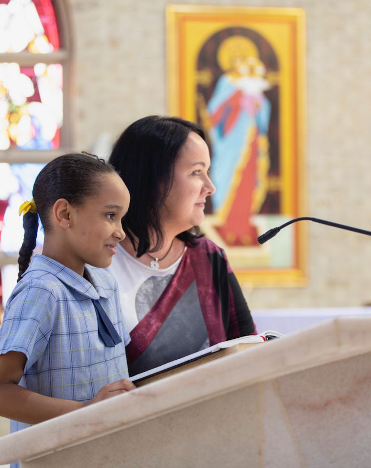 Primary school student speaking at church with teacher.