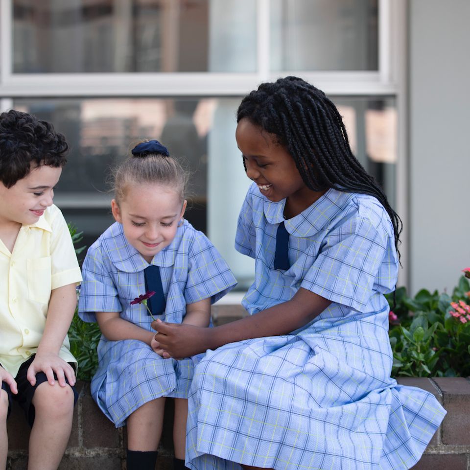 Senior and junior primary school students sitting on brick wall.