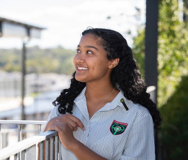 High school student looking out at sky over railing.