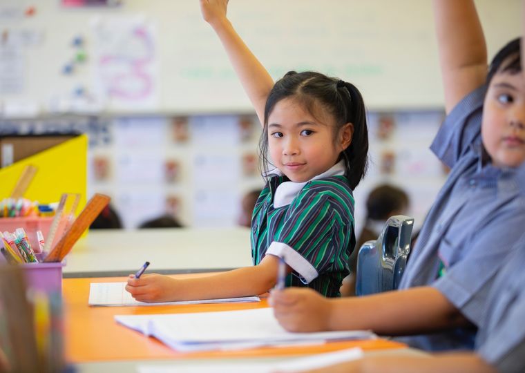 High school students with hands up at desk.