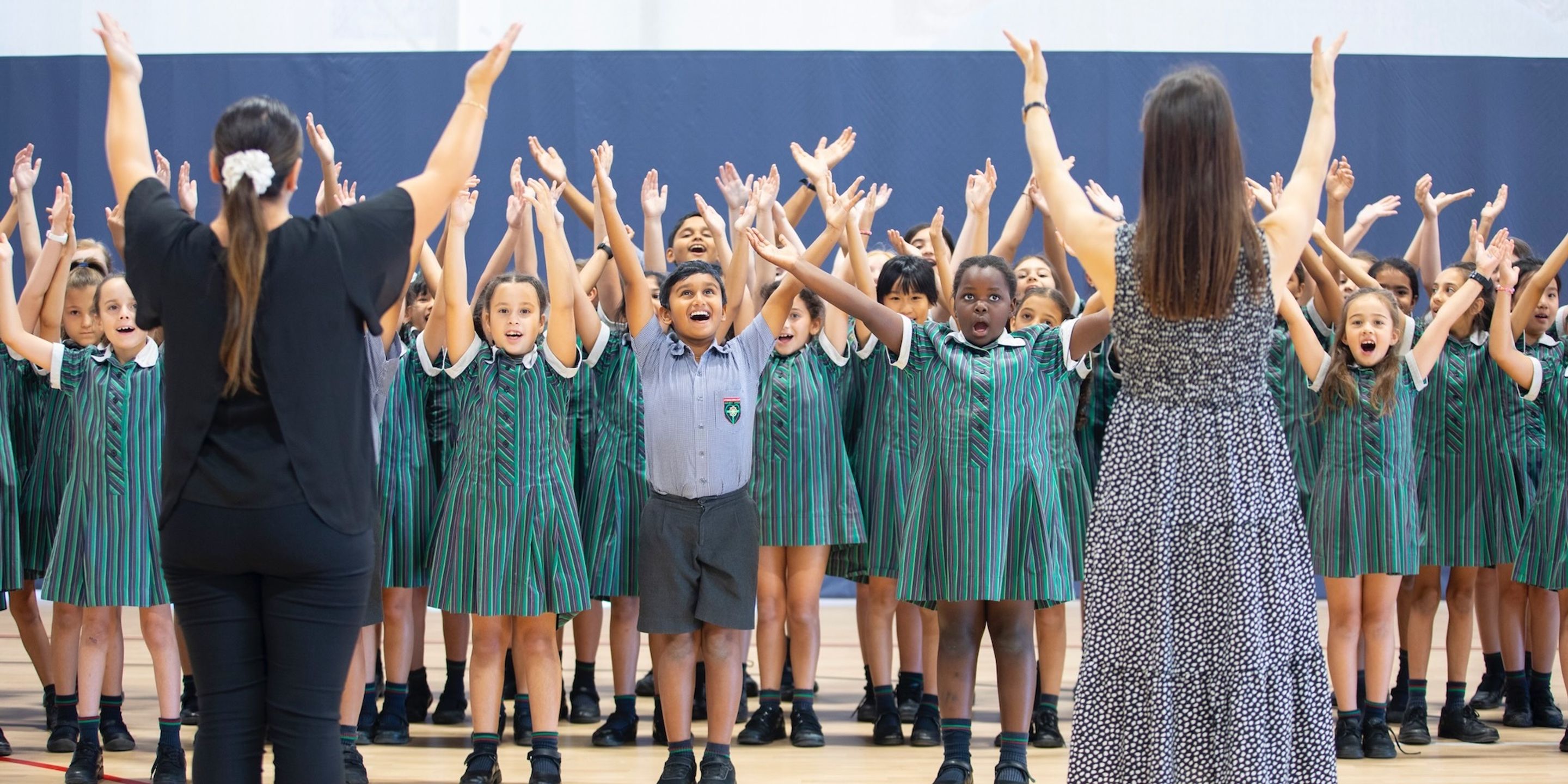 High school students and teachers singing with arms raised.