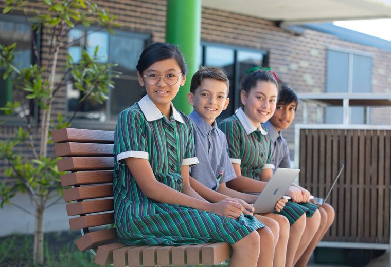 High school students sitting on bench and smiling at camera.