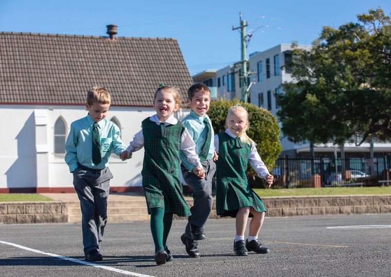 Group of primary school students holding hands and skipping across concrete.