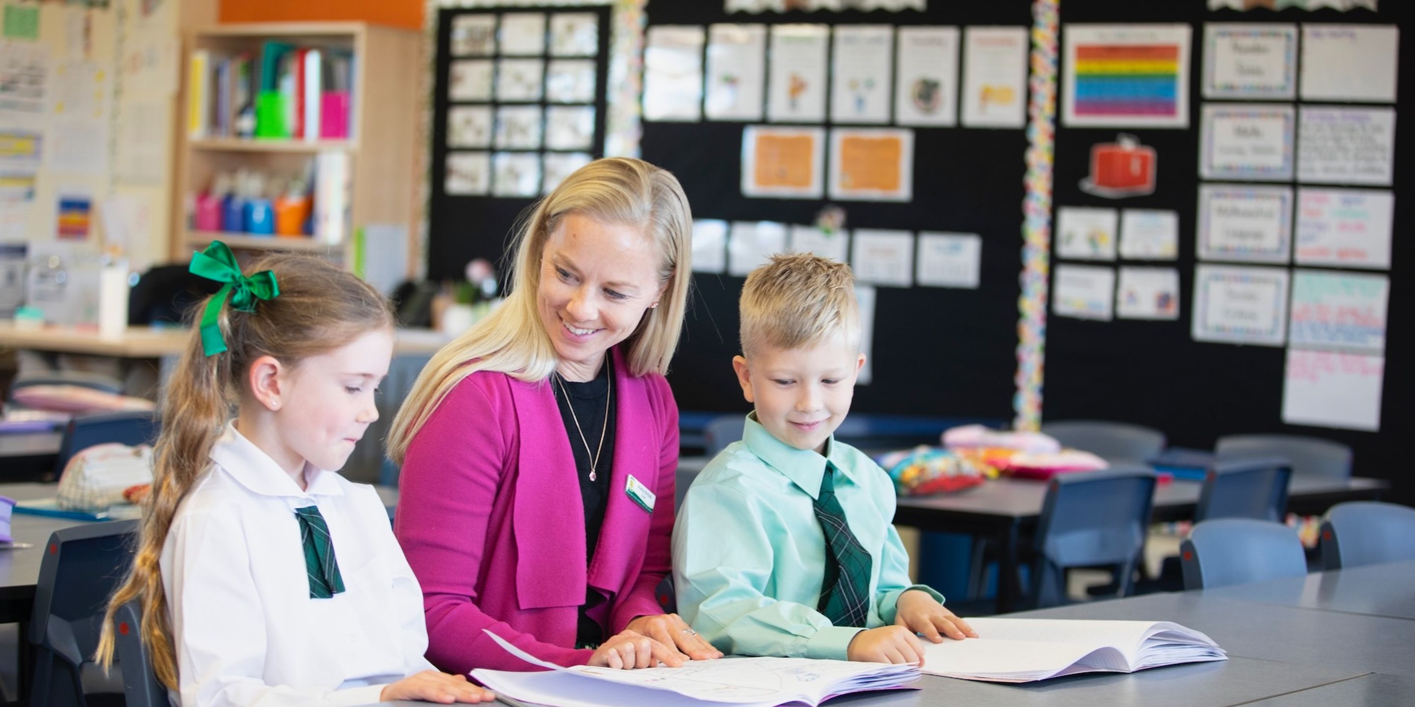 Teacher sitting with two primary school students at school desk.