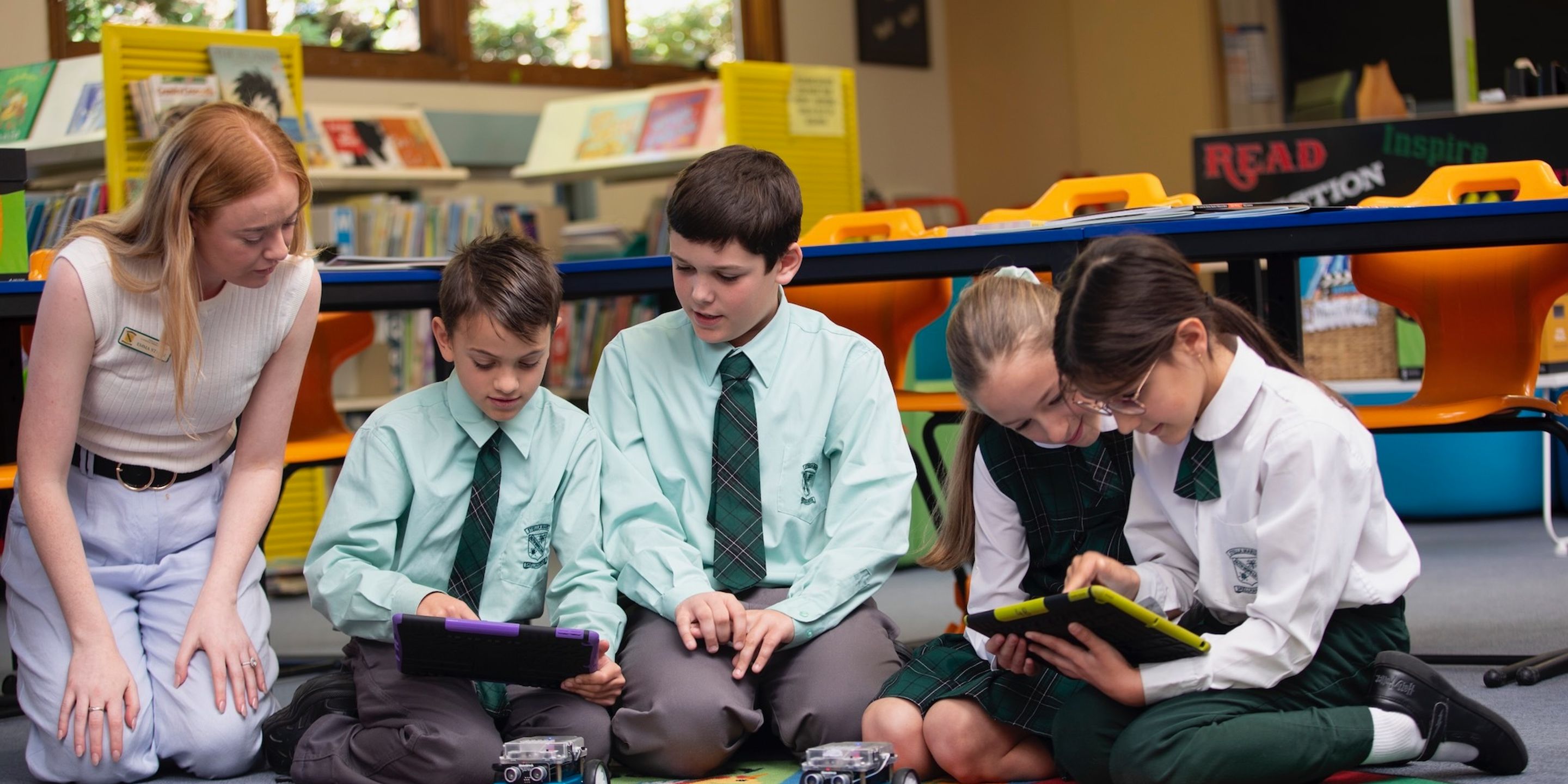 Group of primary school students learning about technology with teacher.