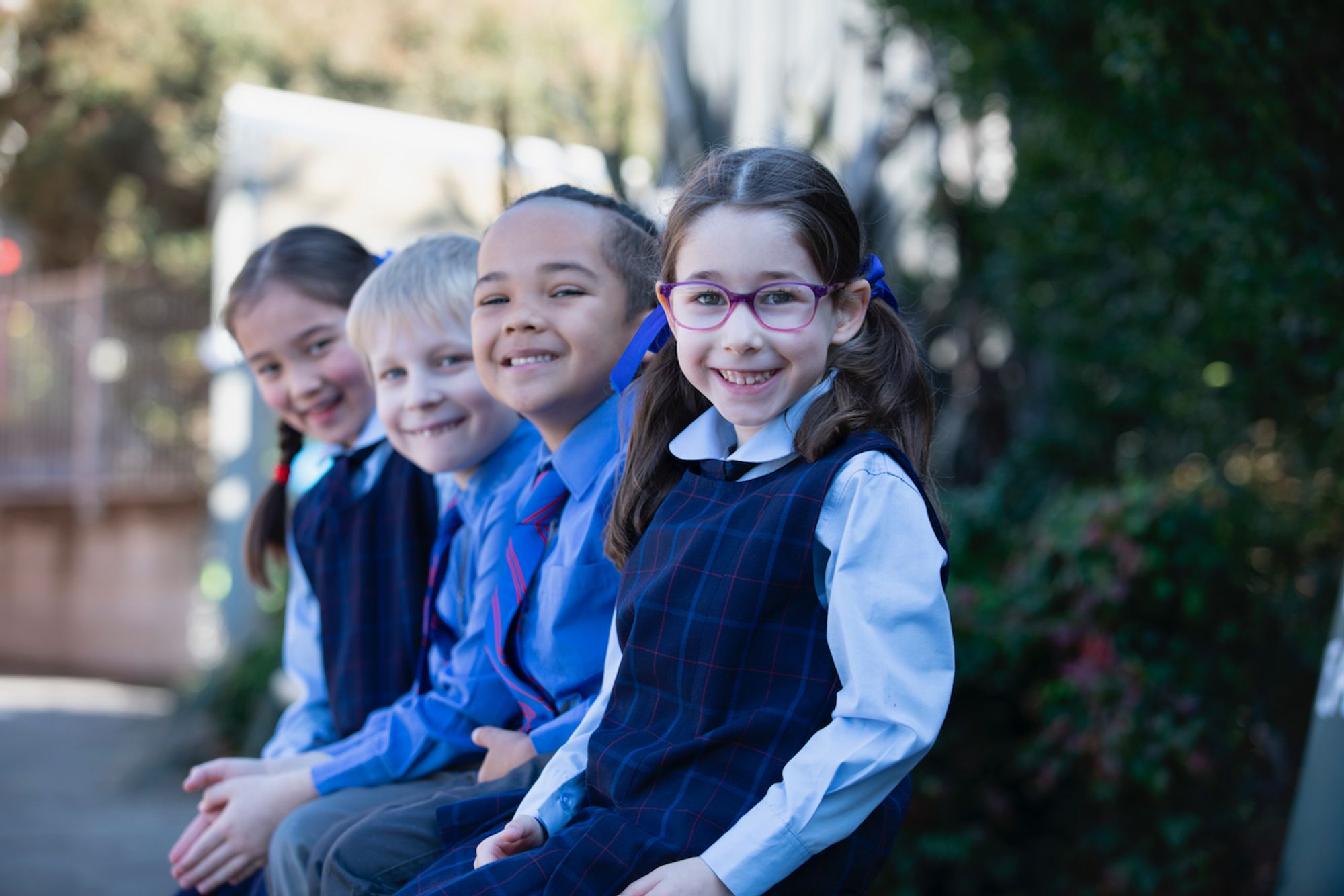 Four primary school students sitting on bench and smiling at camera.