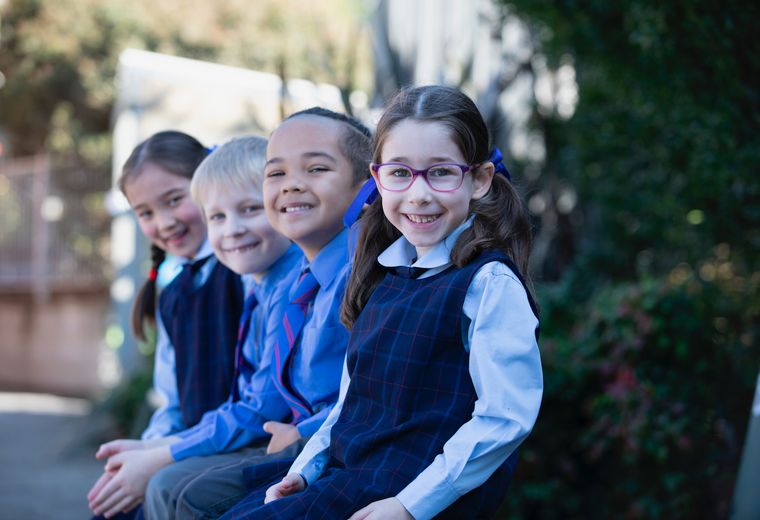 Four primary school students sitting on bench and smiling at camera.