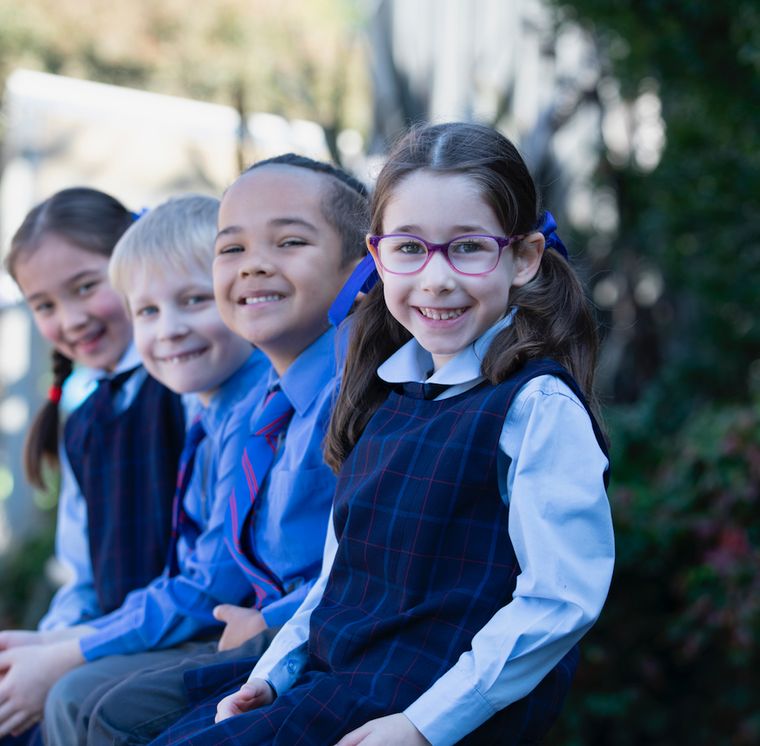 Four primary school students sitting on bench and smiling at camera.