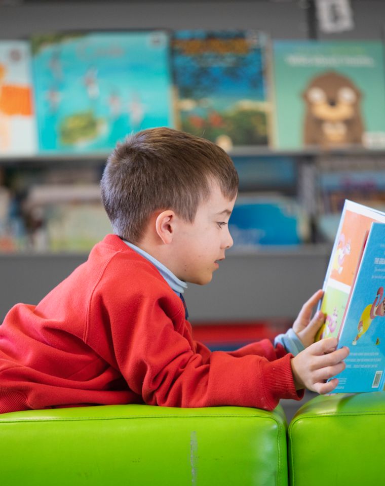 Primary school student reading a book on green ottoman.