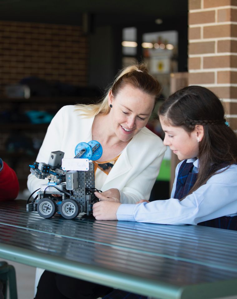 Teacher with two primary school students showing them how to use robots.