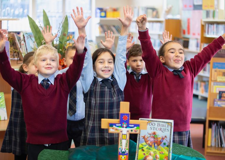 Primary school students smiling with arms up in religion class.