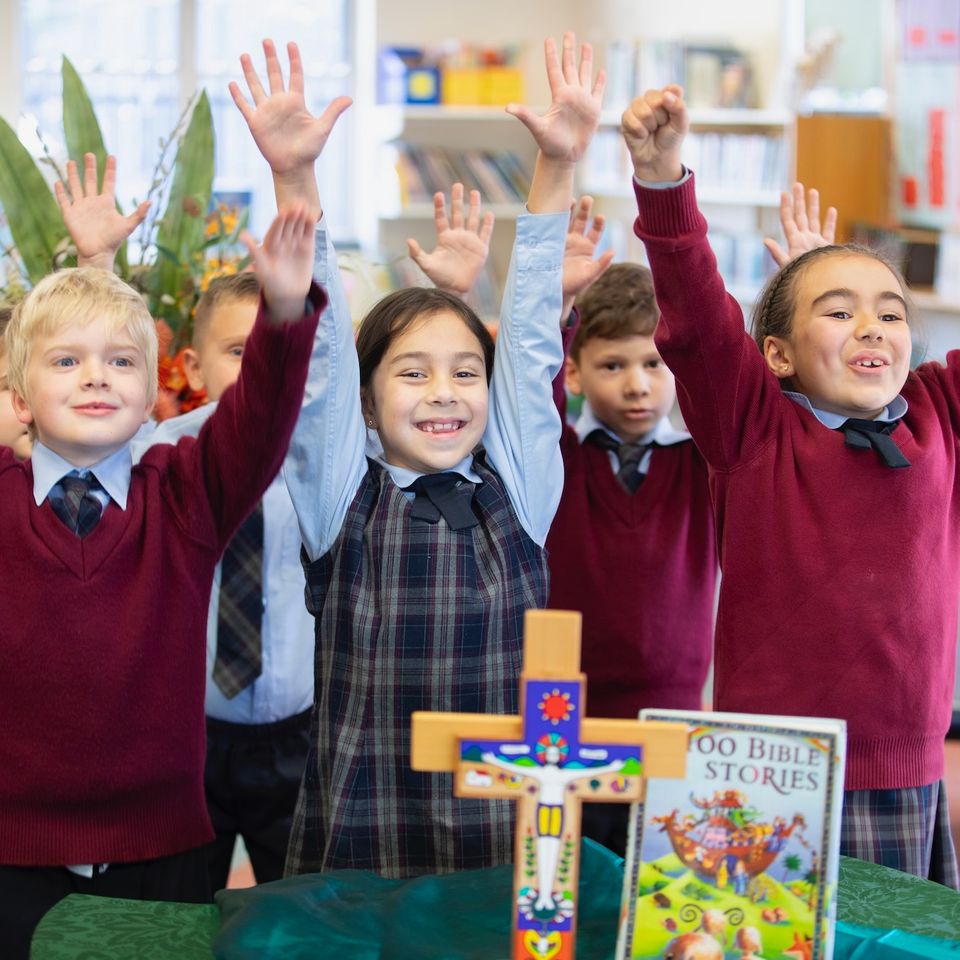 Primary school students smiling with arms up in religion class.