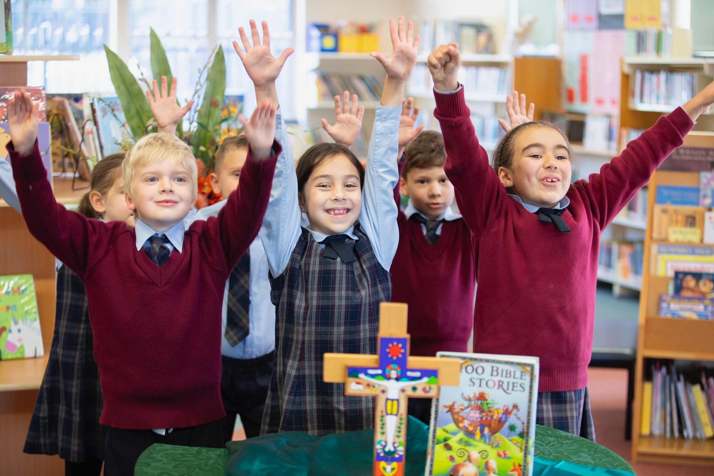 Primary school students smiling with arms up in religion class.