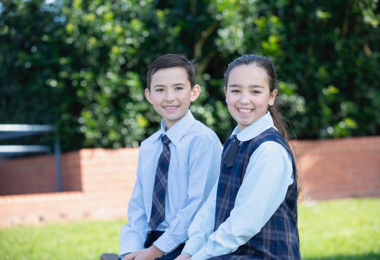 Primary school students sitting on bench outside and smiling at camera.