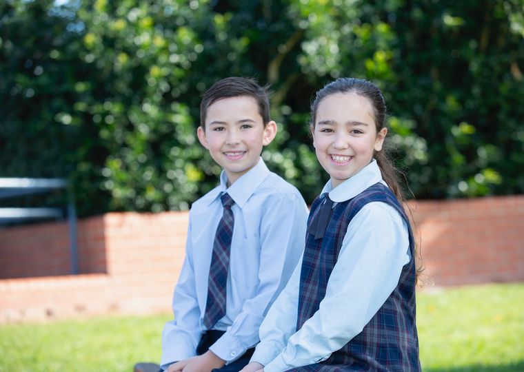 Primary school students sitting on bench outside and smiling at camera.