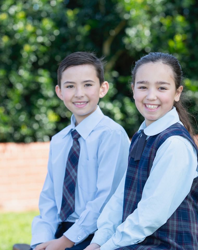 Primary school students sitting on bench outside and smiling at camera.