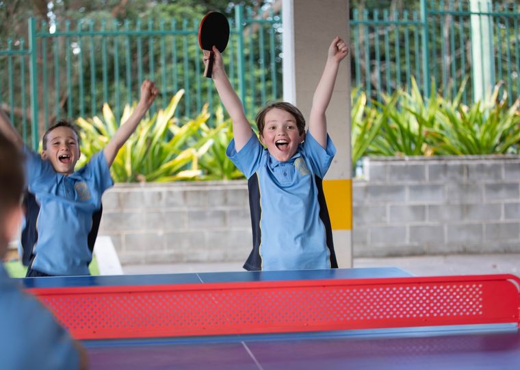 Primary school students cheering during a game of table tennis.