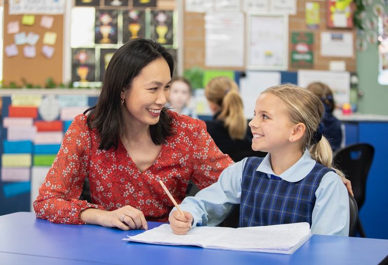 Primary school student doing schoolwork with teacher.