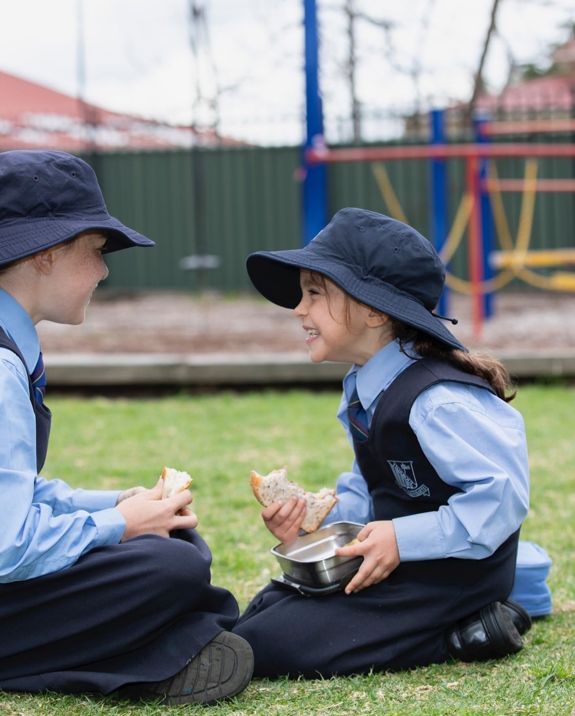 Two primary school students sitting on grass and eating lunch.