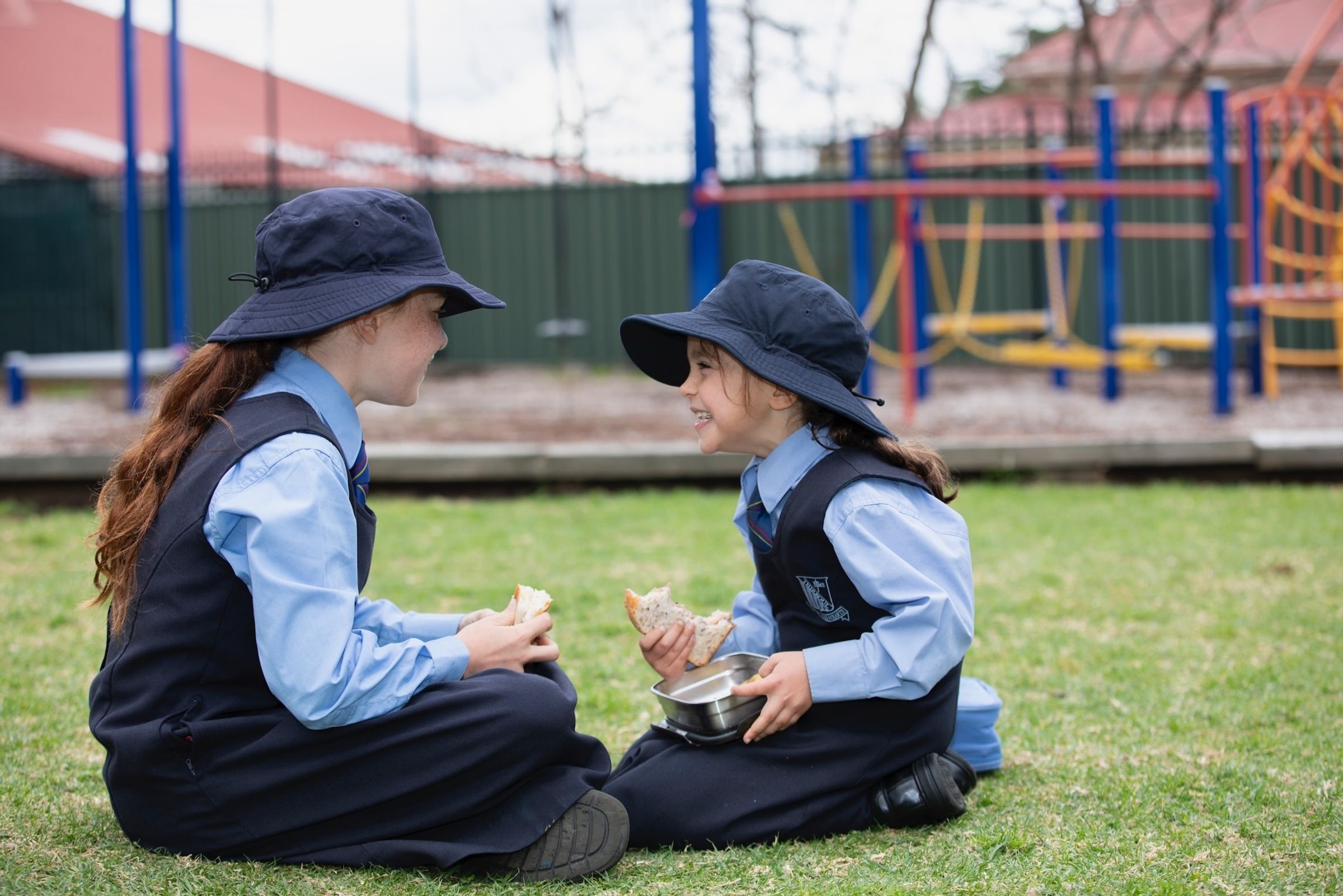 Two primary school students sitting on grass and eating lunch.