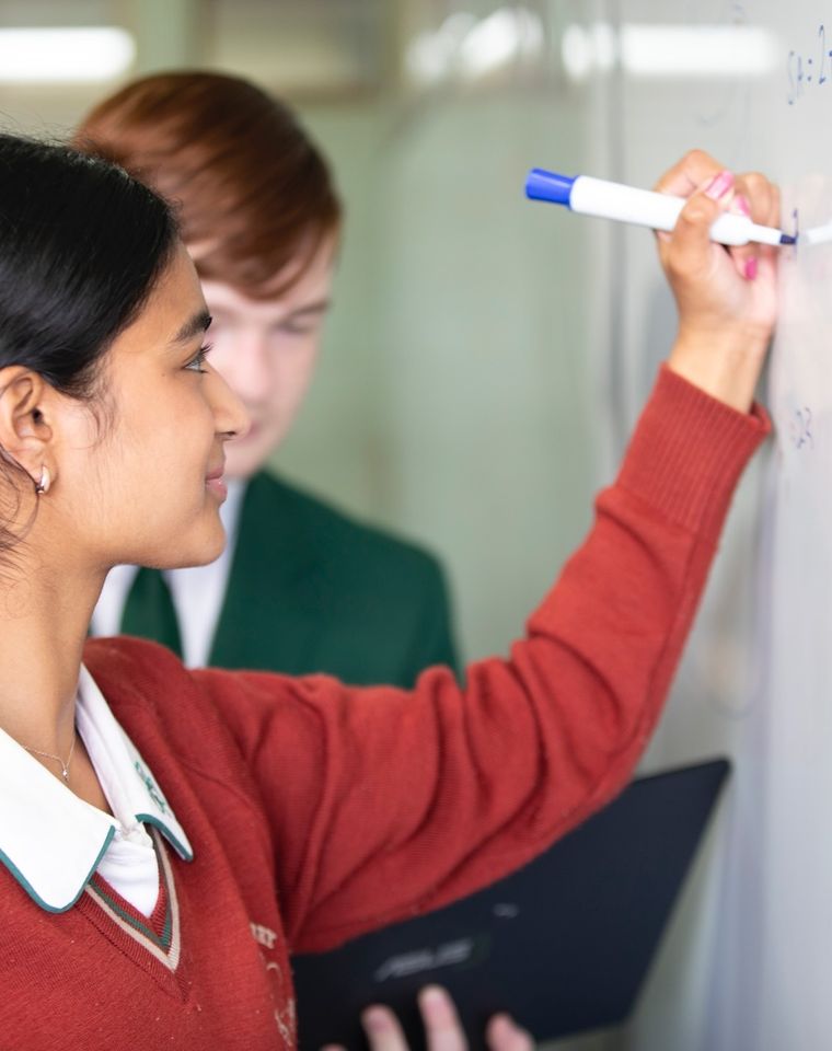 High school student writing on whiteboard.