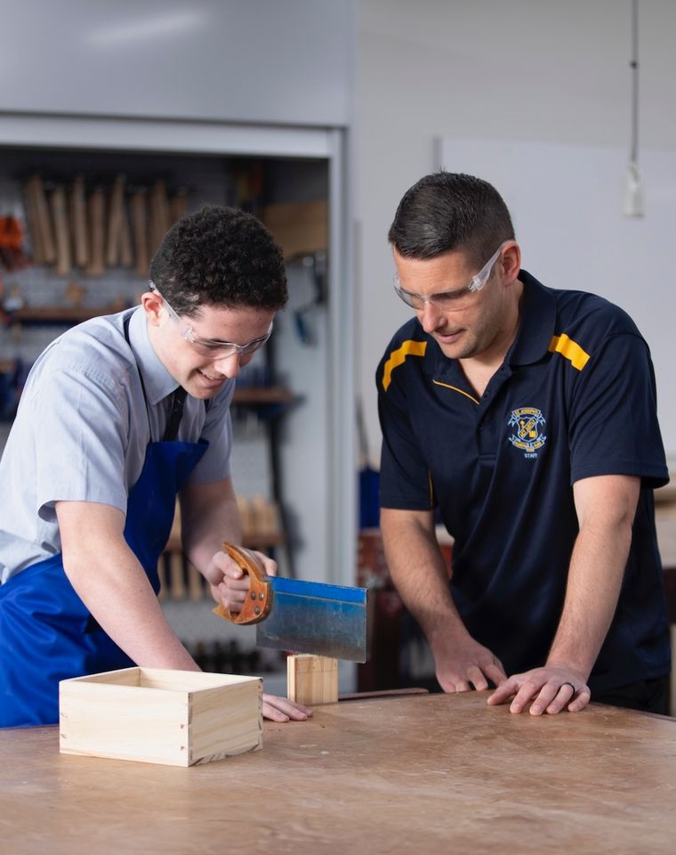 High school student doing woodwork with teacher.