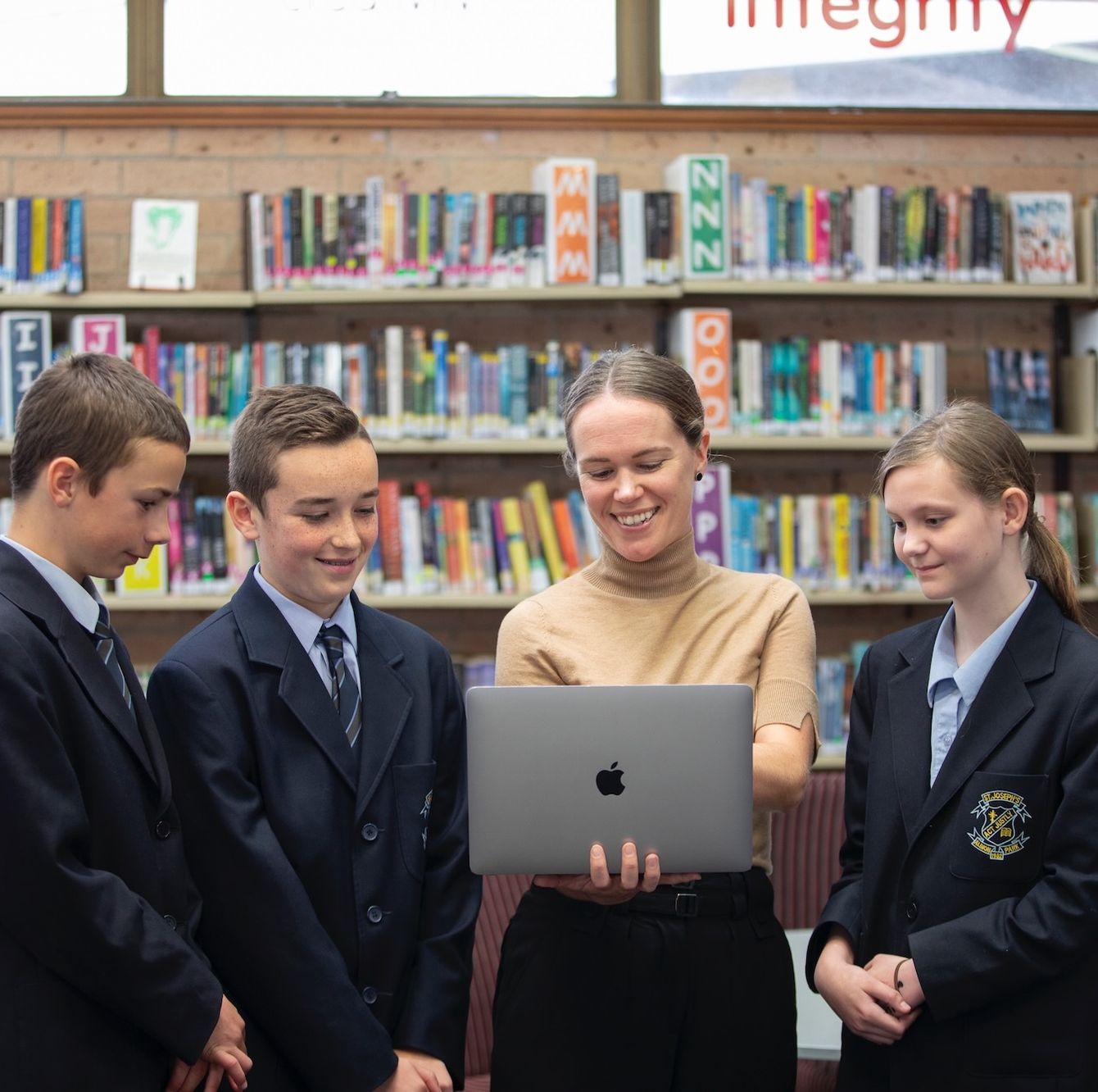 High school students with teacher holding laptop.