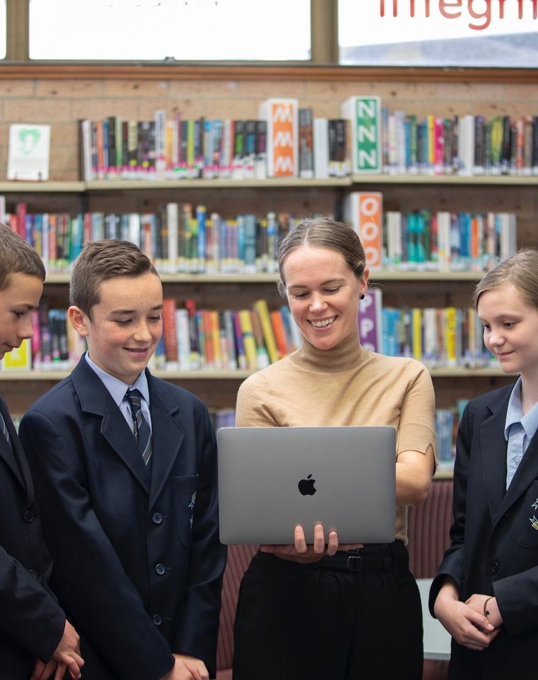 High school students with teacher holding laptop.