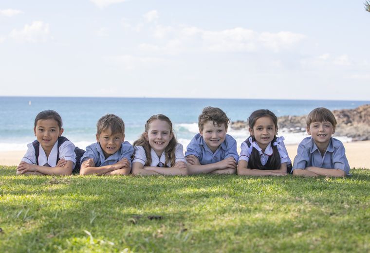 Primary school students on grass outdoors, with beach in background.